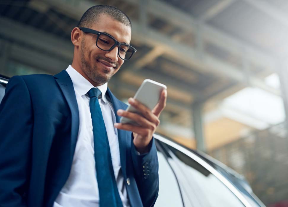 Man in suit standing outside a vehicle looking at mobile phone