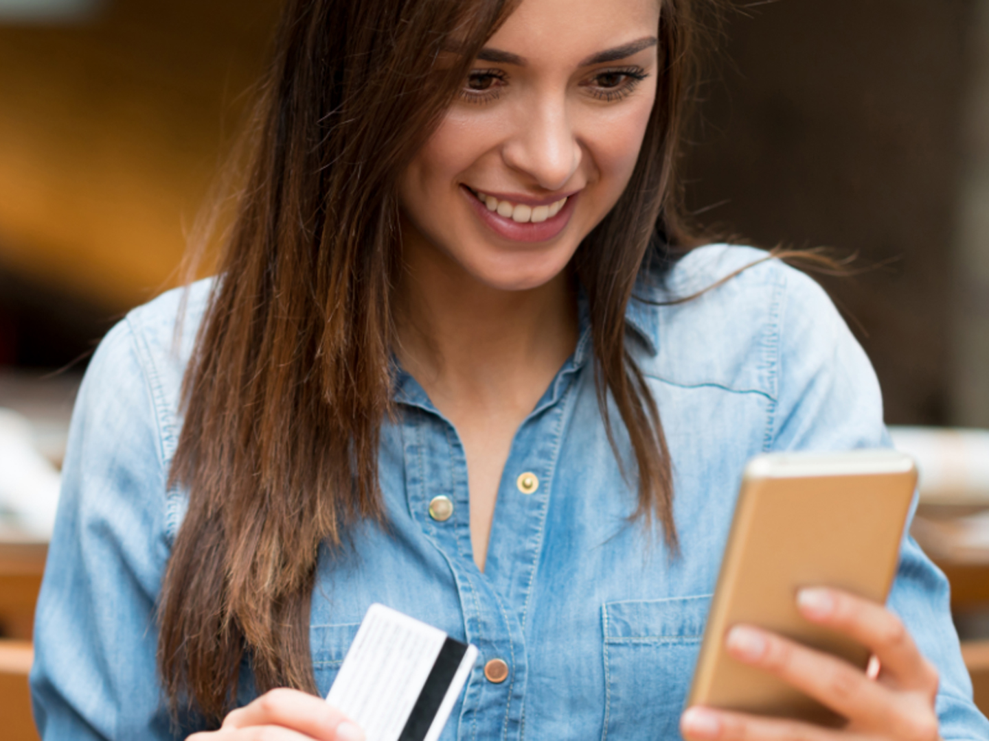 Woman wearing blue shirt looking at mobile phone while holding credit card.
