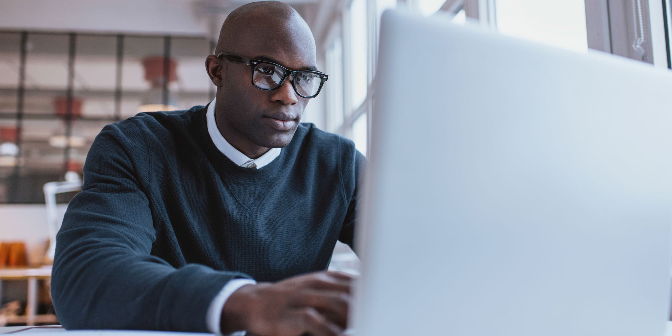 man wearing glasses sitting at his desk working on his laptop