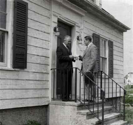 Webster Bank Founder Harold Webster Smith (pictured right with hat in hand) delivers the bank’s first loan to Joe Baltrush in December 1935 on the steps of his home at 114 Chambers Street in Waterbury.